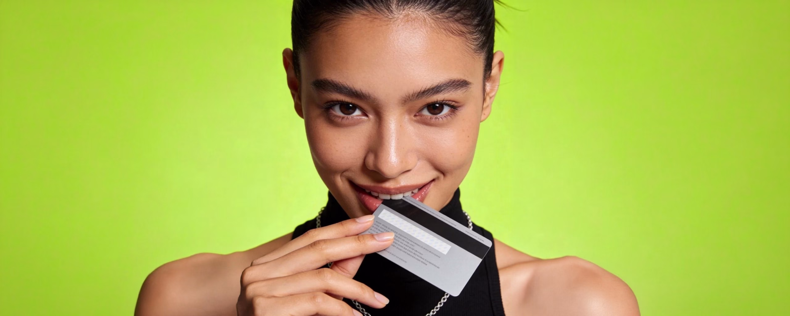 Smiling woman biting a silver credit card against a lime green background